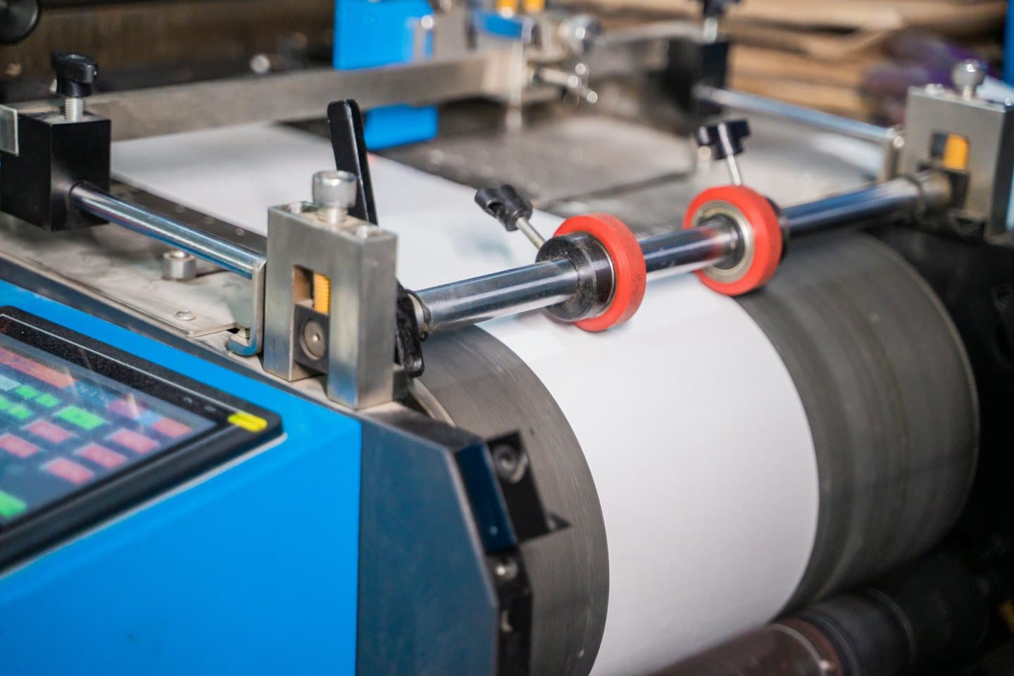Industrial printing press feeding white paper through rollers.