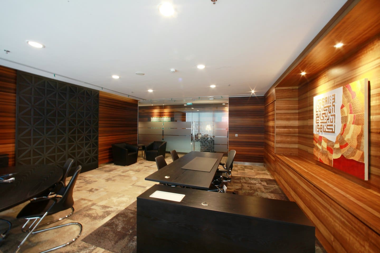 Modern meeting room with wooden furniture and Arabic calligraphy wall art.